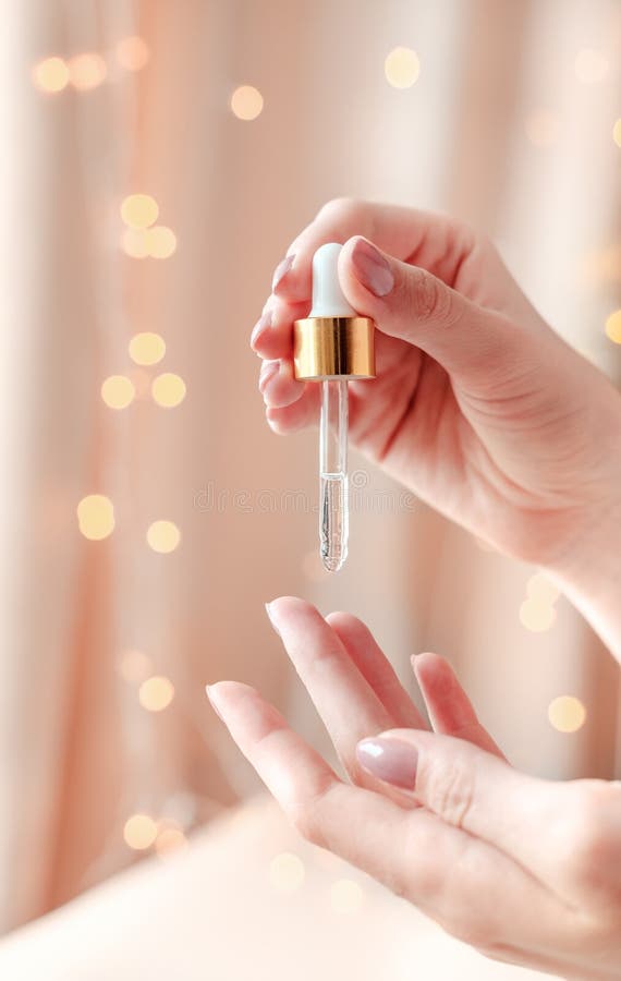 Beautiful groomed woman`s hands with serum on a light bokeh background. Nourishing oil for clean and soft skin