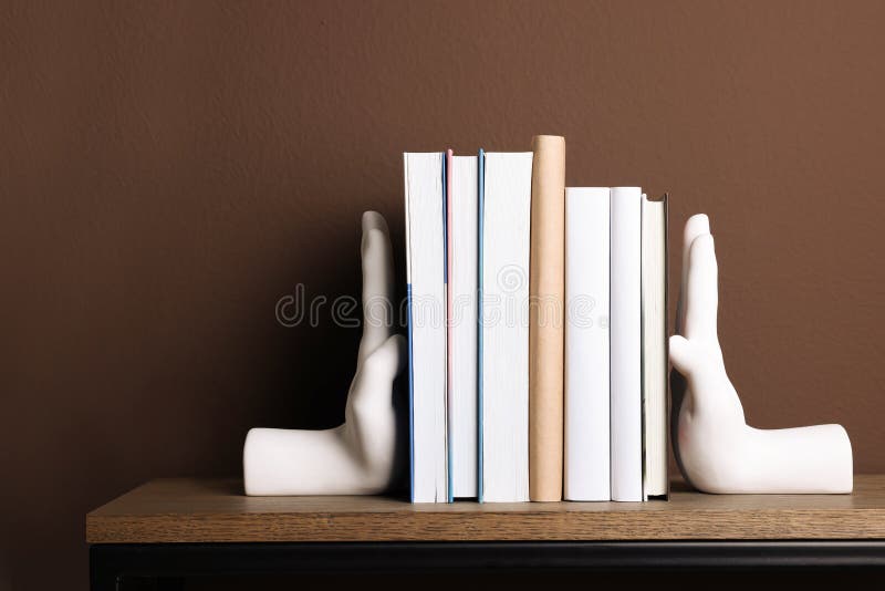Beautiful hand shaped bookends with books on shelf near brown wall