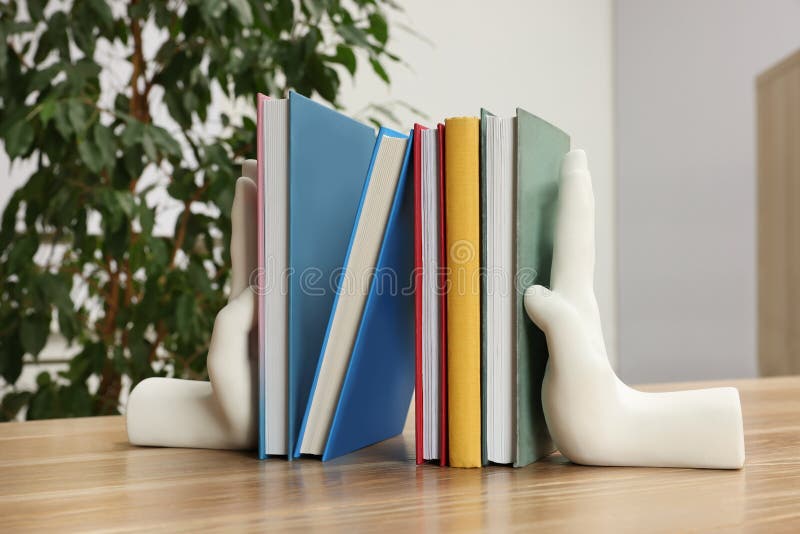 Beautiful hand shaped bookends with books on wooden table indoors