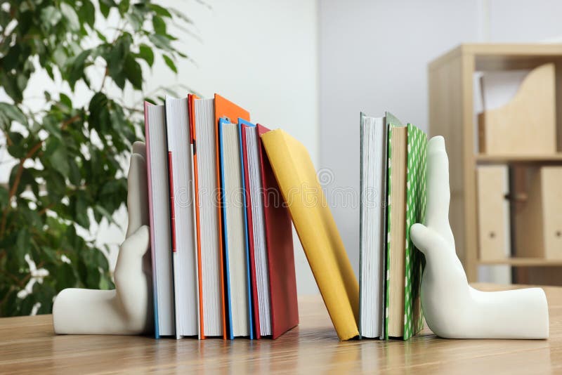 Beautiful hand shaped bookends with books on wooden table indoors