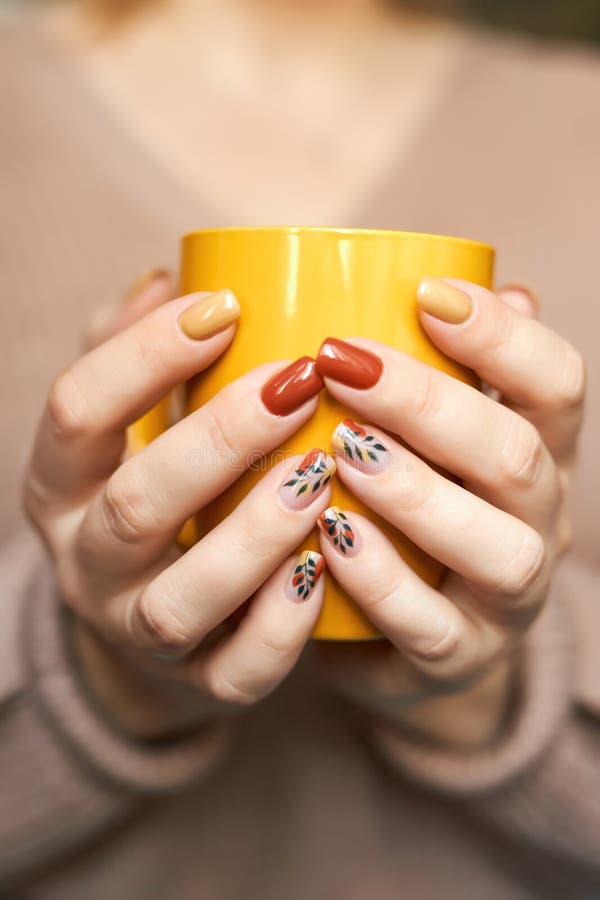 Beautiful hands of a young woman with autumn manicure in brown and yellow colors on nails