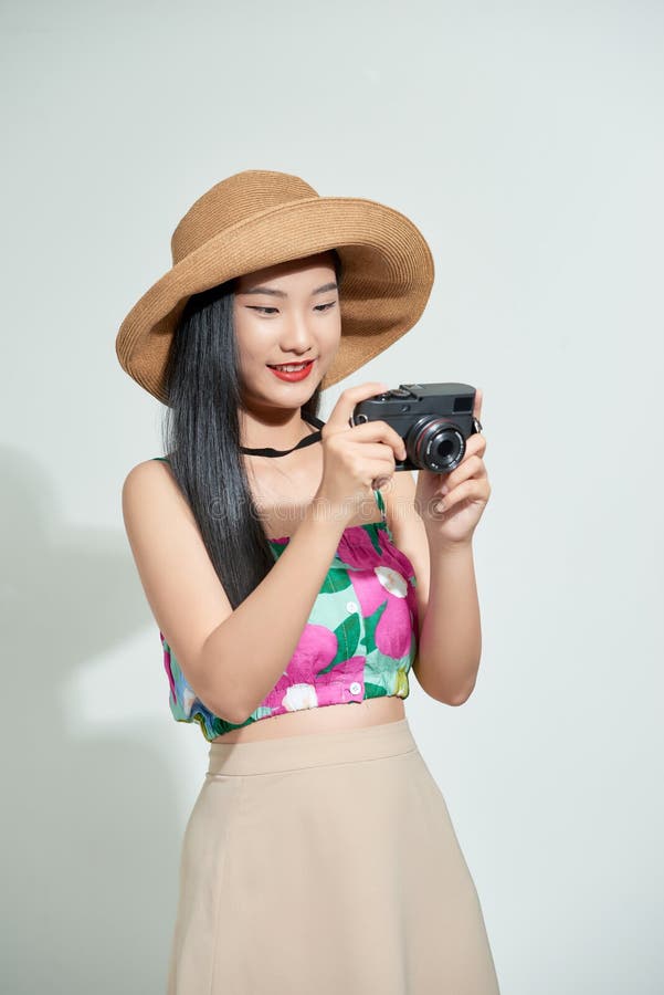 Beautiful happy cute asian woman in casual summer clothes takes photos holding retro photographic camera, isolated on a white in