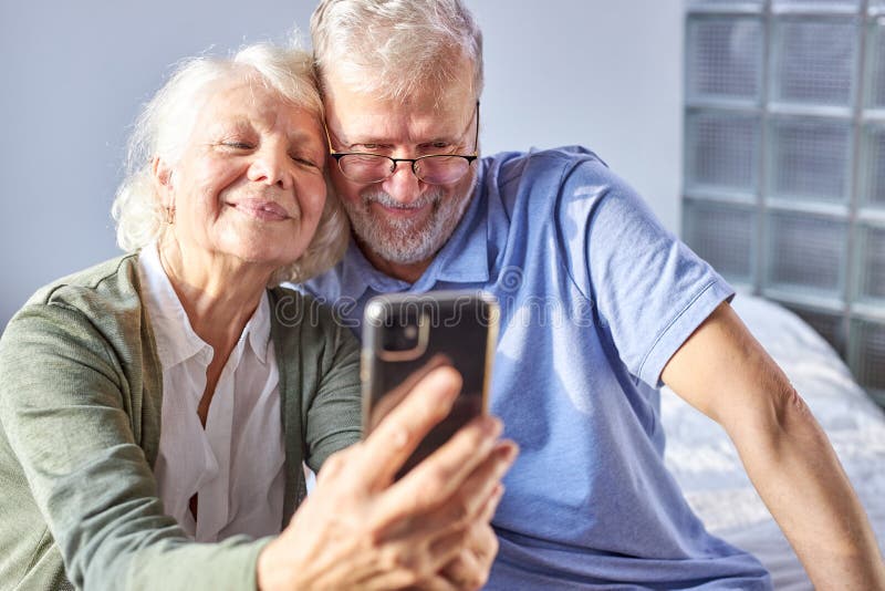 beautiful happy elderly couple taking photo on smartphone stock photography