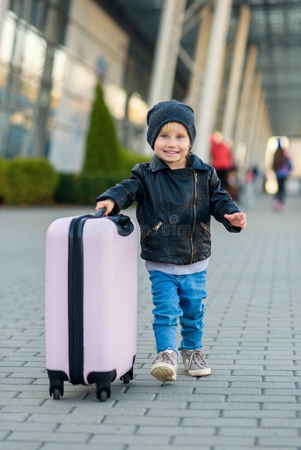 Beautiful happy and joyful girl travels with stylish suitcase. Little child traveler goes to the trip from airport.