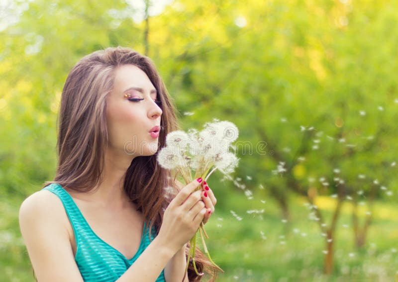 Beautiful happy smiling girl with long dandelions in the hands of shorts and a t-shirt is resting in the Park on a Sunny day