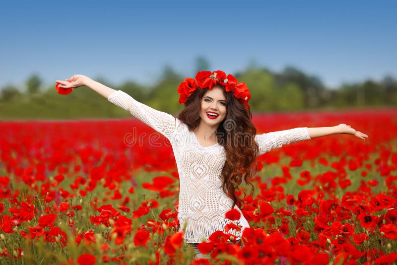 Beautiful happy smiling woman open arms in red poppy field nature background. Attractive brunette young girl model with curly