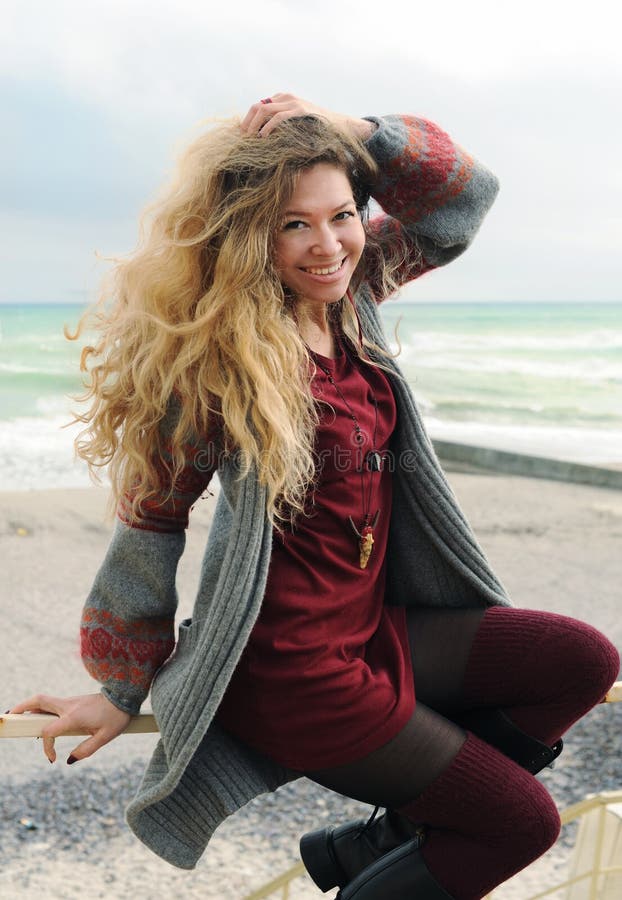 Beautiful happy smiling woman portrait sitting on a banister against autumn sea, long hairs, short fashion dark red dress and gray stock images Beautiful happy smiling woman portrait sitting on a banister against autumn sea, long hairs, short fashion dark red dress and gray stock images