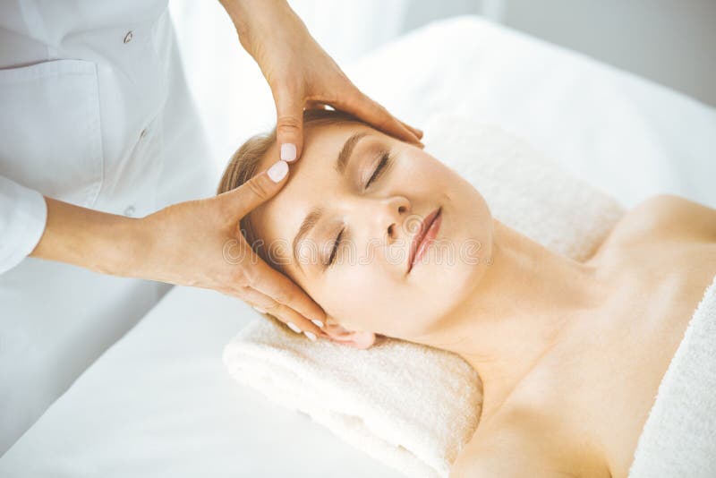 Beautiful Happy Woman Enjoying Facial Massage With Closed Eyes In Spa