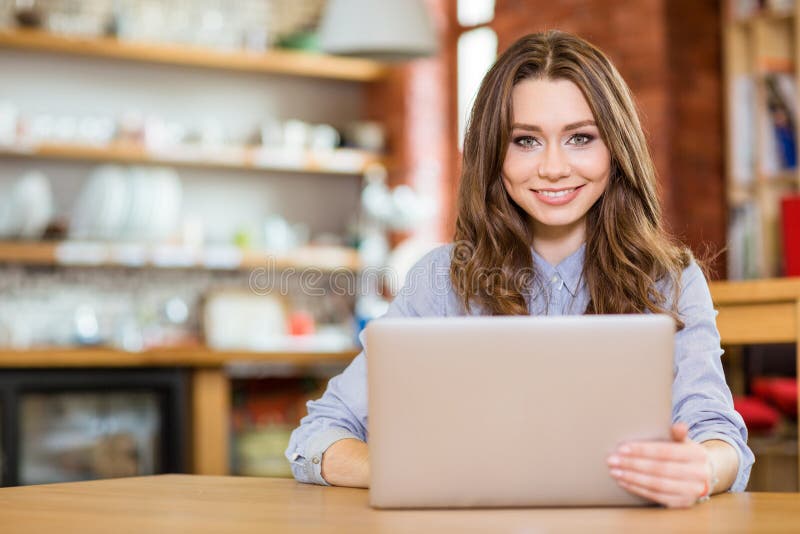 Beautiful happy woman sitting in cafe and using laptop