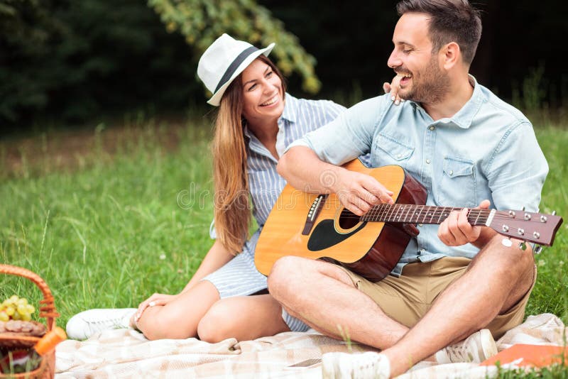 Young couple sitting on a picnic blanket, playing guitar and singing stock images Young couple sitting on a picnic blanket, playing guitar and singing stock images