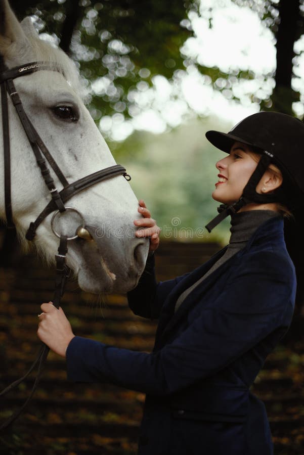 Beautiful horsewoman in blue jacket strokes white horse. royalty free stock image Beautiful horsewoman in blue jacket strokes white horse. royalty free stock image