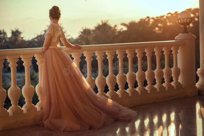 Beautiful lady in luxurious ballroom dress with tulle skirt and lacy top standing on the large balcony