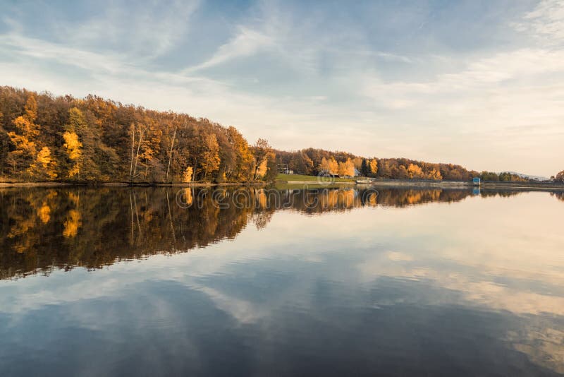 Beautiful lake and colorful forest in autumn evening light. Beautiful forest of colorful autumn trees reflecting in calm lake in D