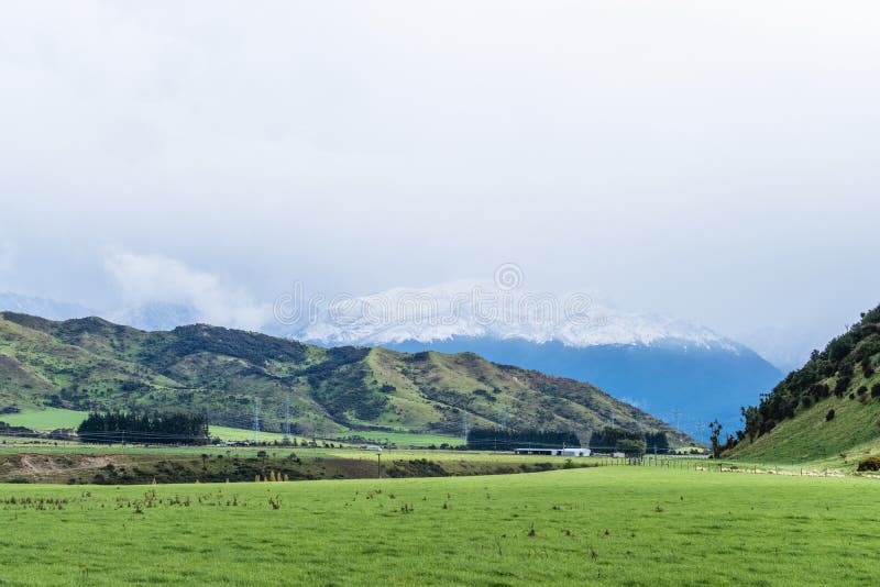 Beautiful Landscape Of A Green Meadows And Snow Mountain In A Cloudy