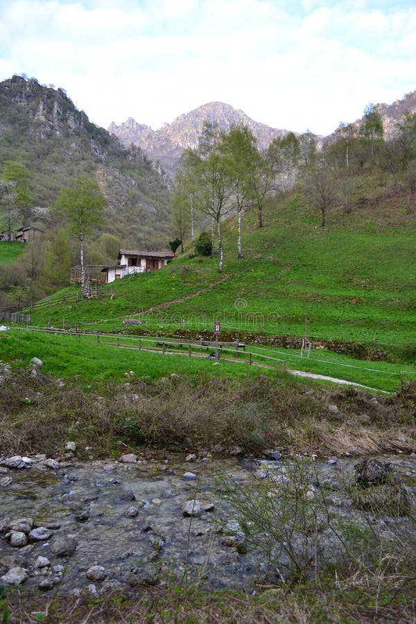 Beautiful landscape in Italian Alps near Lecco with a house, green hills for grazing, stream of water. Beautiful landscape in Italian Alps near Lecco with a stock photography Beautiful landscape in Italian Alps near Lecco with a house, green hills for grazing, stream of water. Beautiful landscape in Italian Alps near Lecco with a stock photography