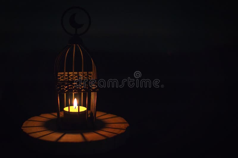 Beautiful Lantern that have moon symbol on top that have light from candle shining on wooden tray with dark background