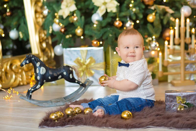 Beautiful little baby boy celebrates Christmas. New Year`s holidays. Baby in a Christmas costume casual clothes with gifts on fur. Room, caucasian.