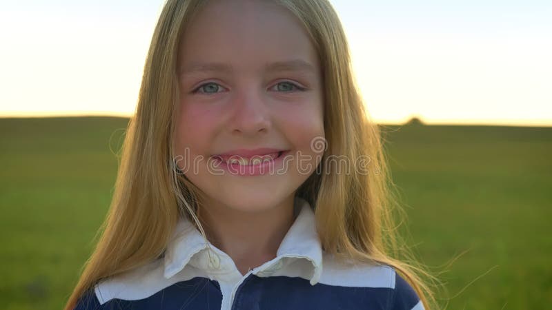 Beautiful little blonde girl turning head towards camera and smiling, cute happy kid with blue eyes standing in wheat