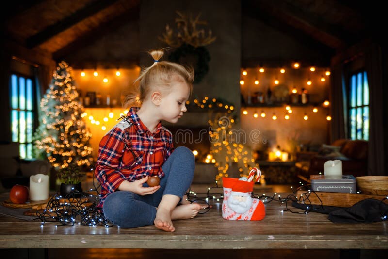A beautiful little blonde in a traditional plaid shirt opens a chocolate bar from her sweet Christmas gift royalty free stock photo A beautiful little blonde in a traditional plaid shirt opens a chocolate bar from her sweet Christmas gift royalty free stock photo