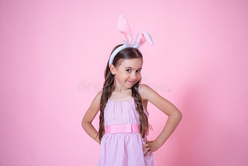 Beautiful little girl dressed in easter bunny ears and in a dress on a pink background