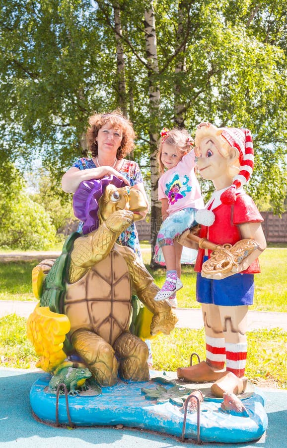 Beautiful little girl with grandmother on the playground with Pinocchio and a turtle royalty free stock photography Beautiful little girl with grandmother on the playground with Pinocchio and a turtle royalty free stock photography