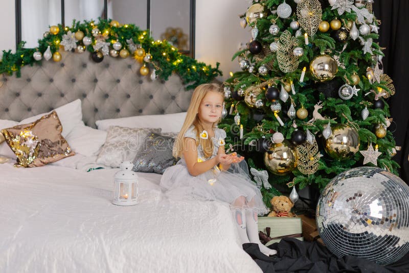 Beautiful little girl holding Christmas candles in her hands while sitting on the bed.