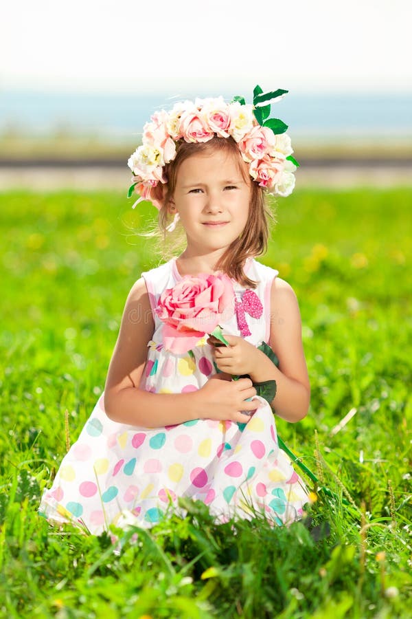 Beautiful little girl with a rose in his hand and a wreath of roses on her head in a field royalty free stock photography Beautiful little girl with a rose in his hand and a wreath of roses on her head in a field royalty free stock photography
