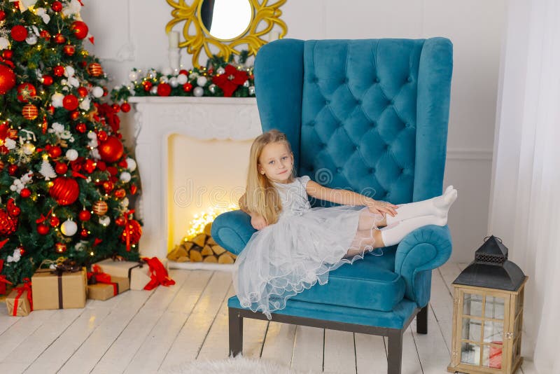 Beautiful little girl sitting on a chair by the tree.