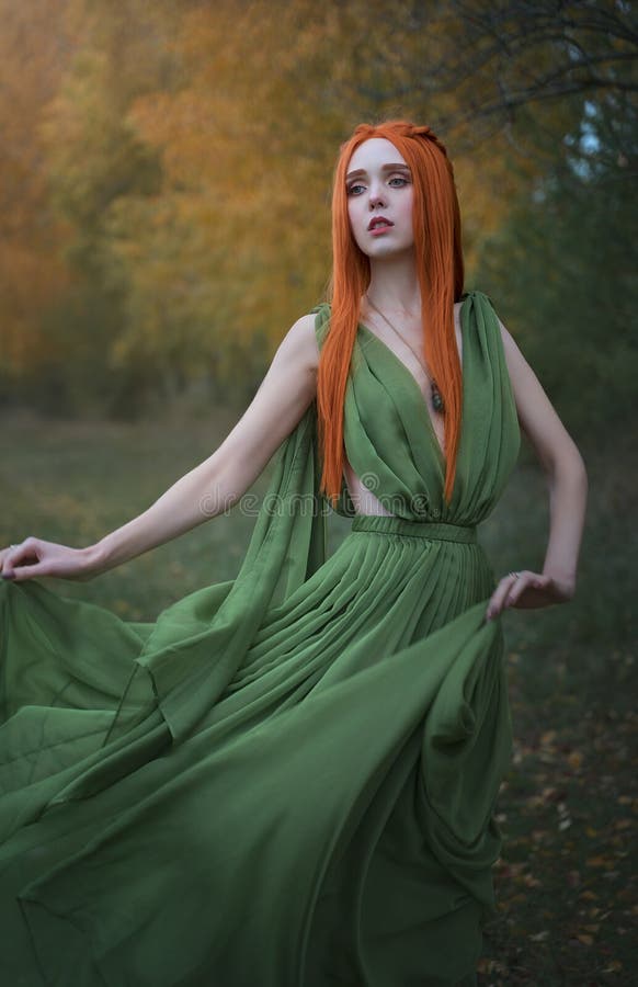 A beautiful long-Haired red-haired elf girl stands in the wind in the autumn forest. A fairy woman with long hair in a