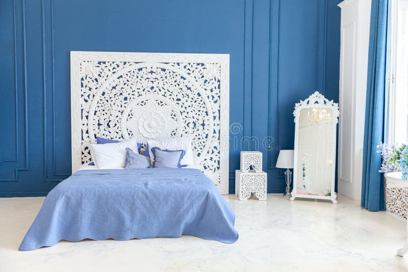 Beautiful luxury classic clean interior bedroom in white and deep blue color with king-size bed and chic carved