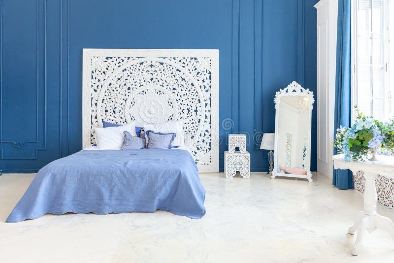 Beautiful luxury classic clean interior bedroom in white and deep blue color with king-size bed and chic carved
