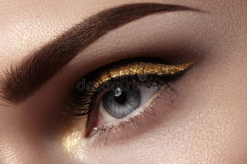 Beautiful macro shot of female eye with ceremonial makeup. Perfect shape of eyebrows, eyeliner and pretty gold line on eyelid
