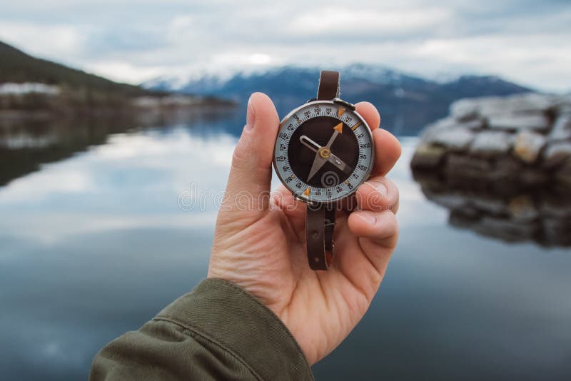 Beautiful male hand holds a magnetic compass against the background of the mountain and a lake. The concept of finding yourself the way and the truth. Beautiful male hand holds a magnetic compass against the background of the mountain and a lake. The concept of finding yourself the way and the truth.