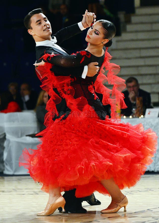 Beautiful man and woman in red dress perform smiling during dancesport competition