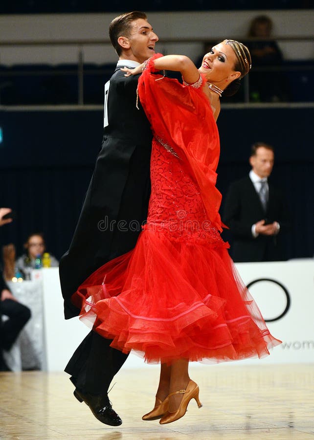 Beautiful man and woman in red dress perform smiling during dancesport competition