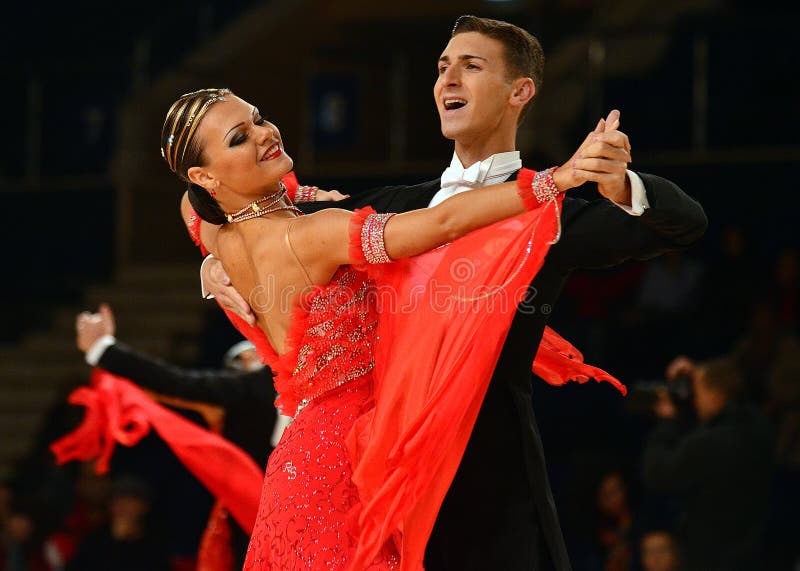 Beautiful man and woman in red dress perform smiling during dancesport competition