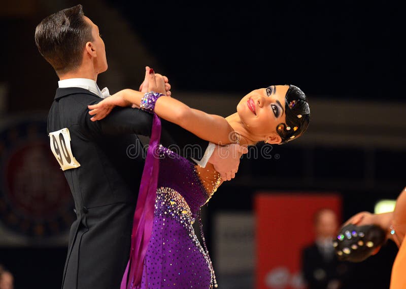 Beautiful man and woman in violet dress perform smiling during dancesport competition