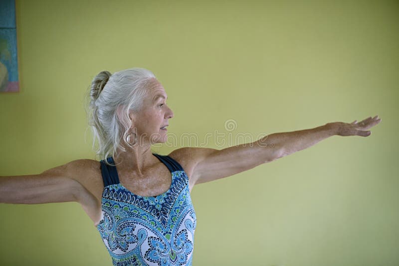 Beautiful mature senior woman in a perfect yoga pose with her arms stretched out in warrior pose. `Aging is not `lost youth` but a new stage of opportunity and strength.` -Betty Friedann`There is a fountain of youth: it is your mind, your talents, the creativity you bring to your life and the lives of the people you love. When you learn to tap this source, you will truly have defeated age.` -Sophia Loren. Beautiful mature senior woman in a perfect yoga pose with her arms stretched out in warrior pose. `Aging is not `lost youth` but a new stage of opportunity and strength.` -Betty Friedann`There is a fountain of youth: it is your mind, your talents, the creativity you bring to your life and the lives of the people you love. When you learn to tap this source, you will truly have defeated age.` -Sophia Loren