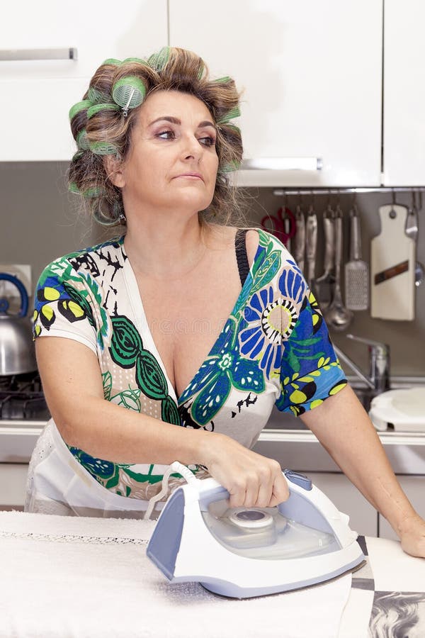 Beautiful mature woman with curlers ironing stock photo.