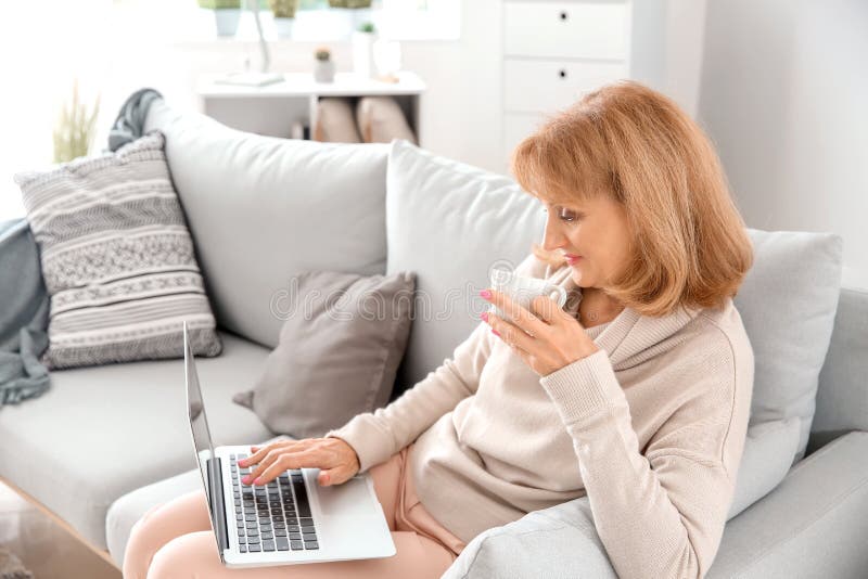 Beautiful mature woman drinking coffee while using laptop at home