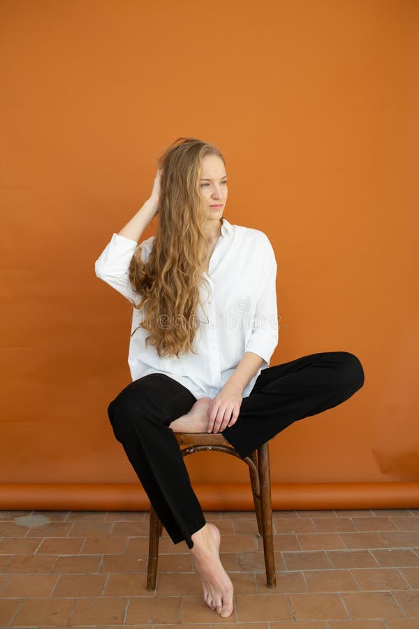 Beautiful model on orange background sitting on the chair in white shirt and black trousers stock images Beautiful model on orange background sitting on the chair in white shirt and black trousers stock images
