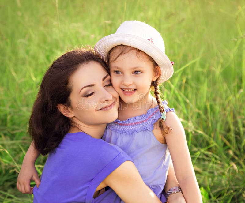 Beautiful mother hugging and kissing her cute small daughter on summer green grass background. Closeup royalty free stock images Beautiful mother hugging and kissing her cute small daughter on summer green grass background. Closeup royalty free stock images