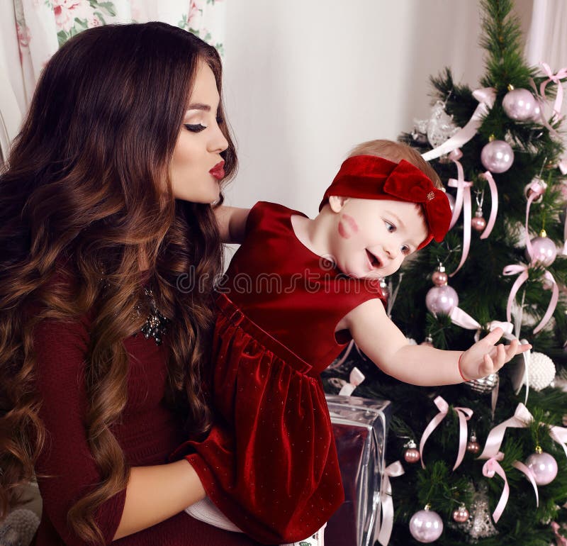 Beautiful mother with luxurious dark hair posing with her cute little girl beside Christmas tree