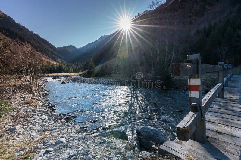 Beautiful mountain stream and peak landscape with the sun shining and a wooden bridge with a hiking trail sign in the foreground royalty free stock images Beautiful mountain stream and peak landscape with the sun shining and a wooden bridge with a hiking trail sign in the foreground royalty free stock images