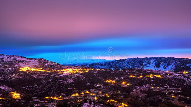 Beautiful mountains landscape, amazing pink and blue sky over mountainous glowing city, beauty of nighttime, winter holidays concept