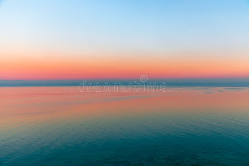 Beautiful multicolor sunset reflected in the waters of Lake Garda, Italy. Skyline. Visible coastline in the evening fog. Winter