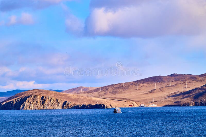 Beautiful natural view of the landscape with the shore with yellow grass, lake, blue sky and mountains or hills on