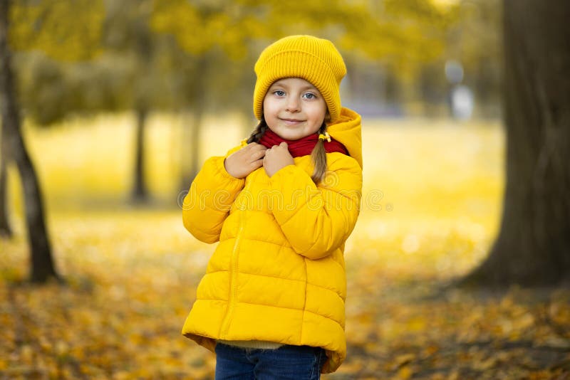 Beautiful outdoor autumn portrait of adorable 4-years old child girl, wearing stylish yellow cap and coat, touching her
