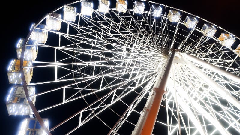 Beautiful image of ferris wheel on city stret illuminated with white bulbs with night sky on the background