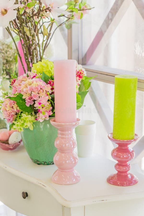 Beautiful pink flowers in green vase and Candles on white wooden  commode.